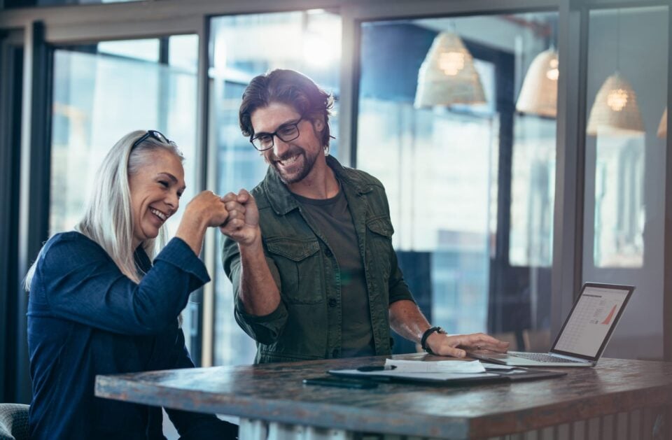 Young businessman and senior businesswoman making a fist bump at office. Business colleagues looking happy and excited after completion of project.